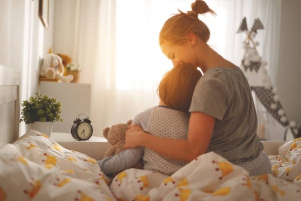 Maternidad consciente; mujer abrazando a su hijo sentados en una cama